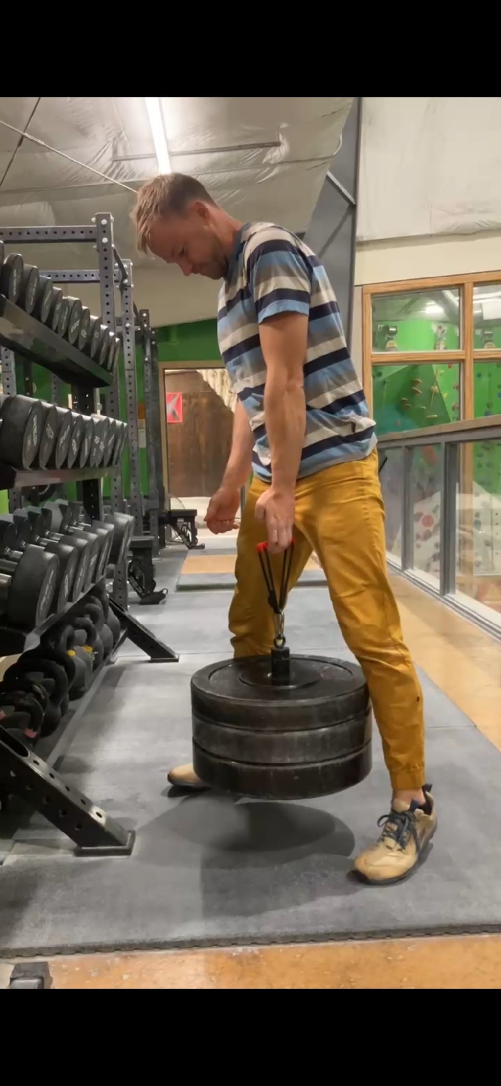 A man in a gym wearing a blue and white striped t-shirt and mustard yellow pants, using The Minimalist with a loading pin stacked with 135 lbs. (61 kg)