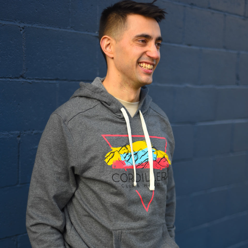 Man wearing a gray hoodie with colorful design against a blue brick wall