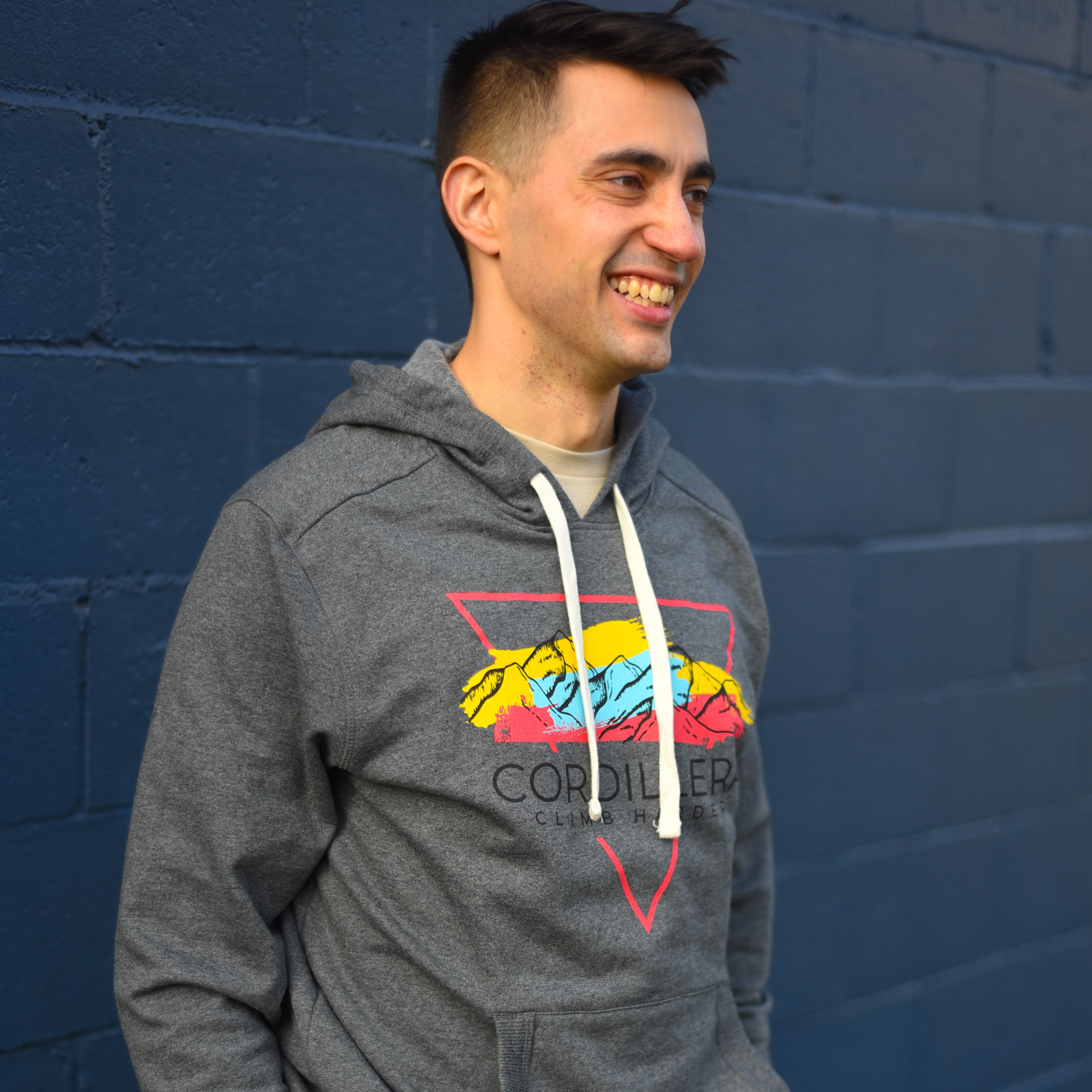 Man wearing a gray hoodie with colorful design against a blue brick wall