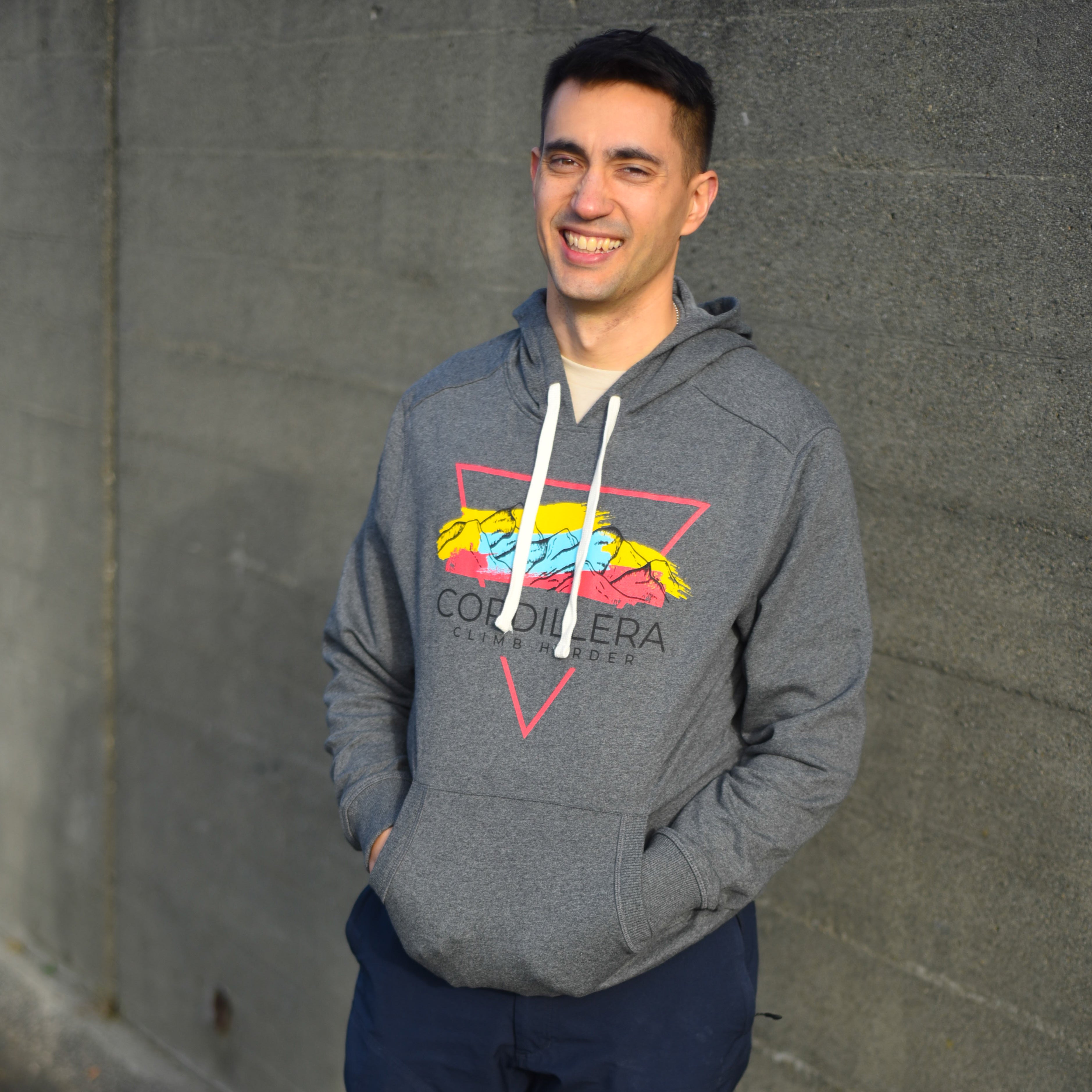 Man wearing a gray hoodie with a colorful logo against a gray wall