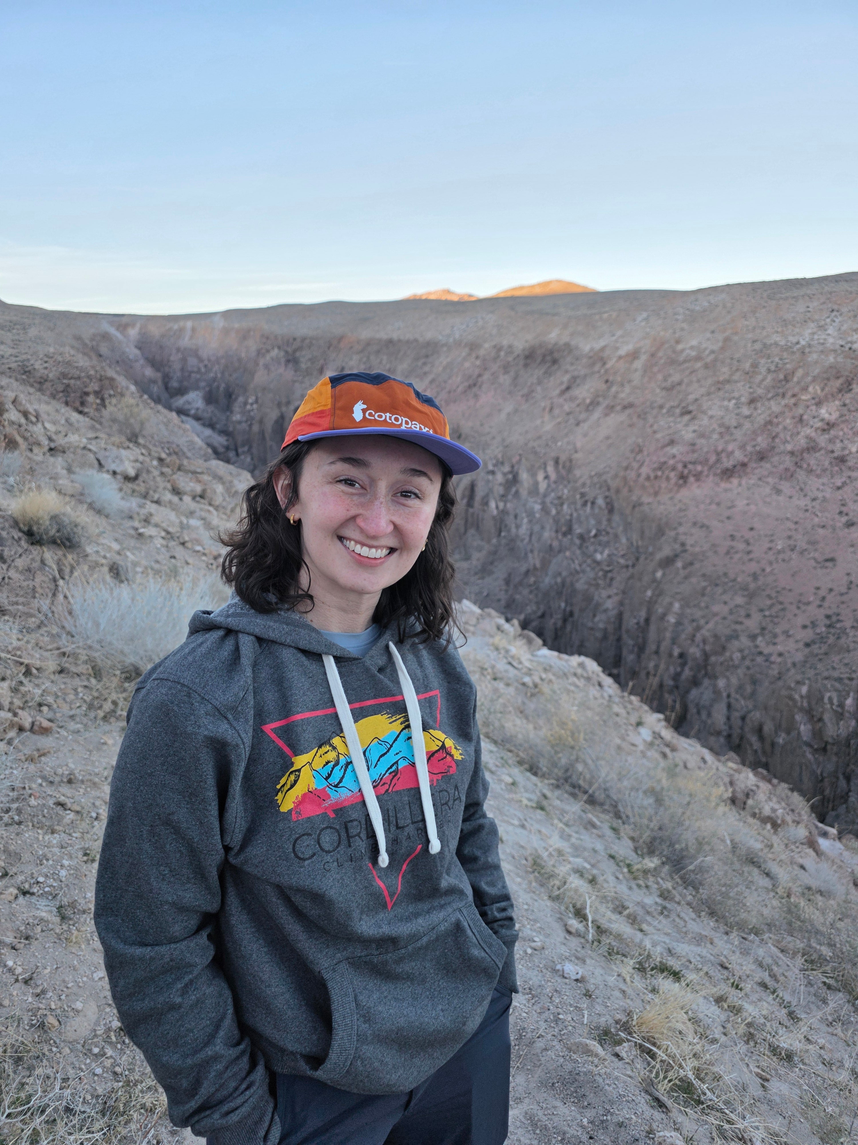 Person wearing a gray hoodie with colorful graphics and an orange cap standing on a rocky surface.